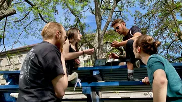 Vier Personen sitzen, reden auf Parkbänken.