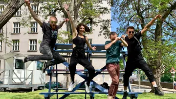 Four people jump from blue bleachers outside.