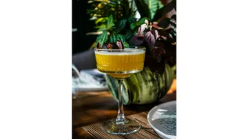 Gelber Cocktail garniert auf Holztisch.