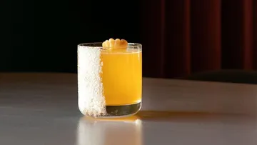 Glas mit orangefarbenem Getränk, Kokosrand, Tisch.