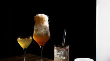 Drei Cocktails auf Holztisch, dunkler Hintergrund.
