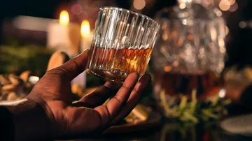 Hand hält ein Glas Whiskey, Kerzen in der Nähe.