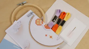 Stickrahmen mit Garnen und Nadel auf Tisch.