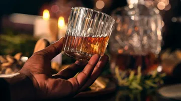 Hand hält Glas mit Whiskey, warme Atmosphäre.