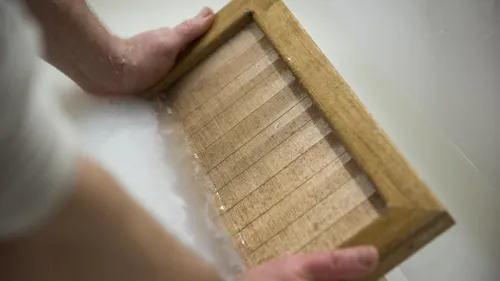 Hände machen Papier mit Holzrahmen.