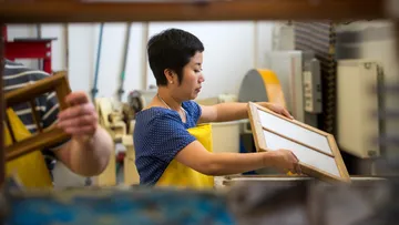 Person holding paper-making frame in workshop.