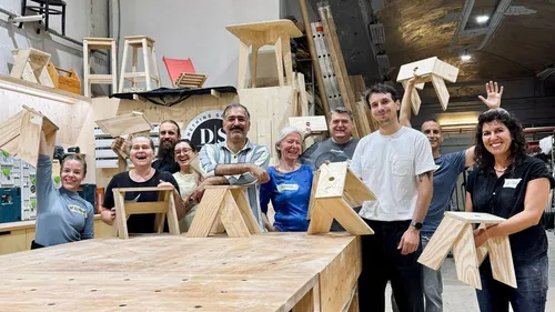 Gruppe hält Holzstühle, Werkstattumgebung.
