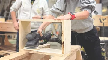 Person schleift Holzrahmen in Werkstatt.