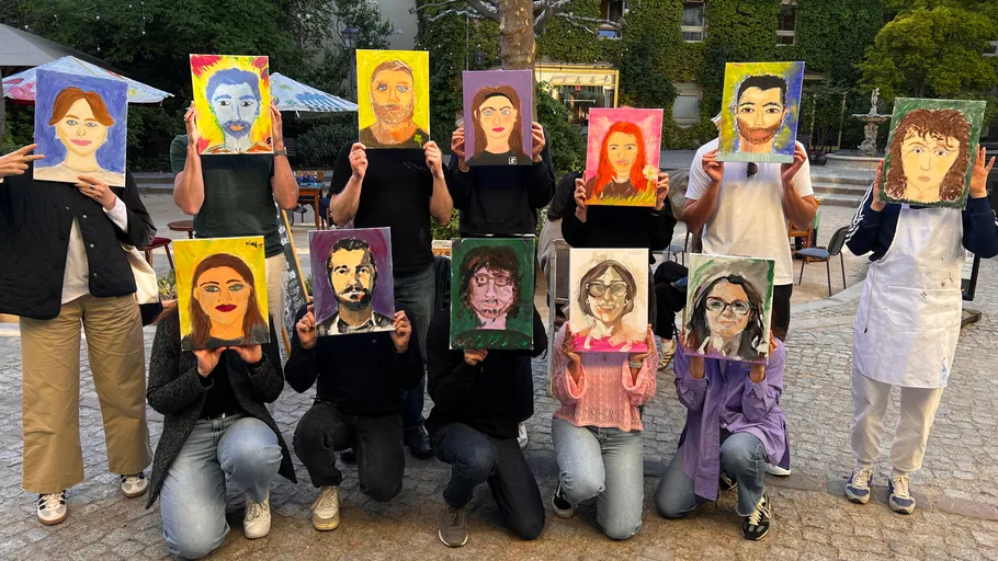People holding colorful self-portrait paintings outdoors.