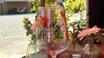 Weinglas mit 'holy Aperoly' Text draußen.