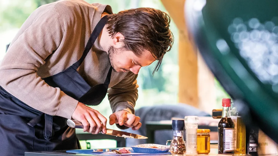 Man cuts ingredients in an outdoor kitchen.
