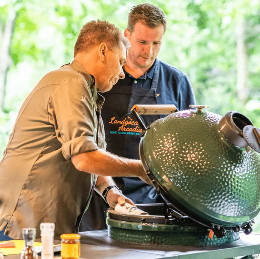 Green grill is opened while two people work together.