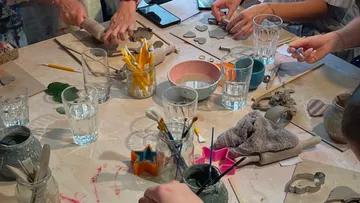 Hände formen Ton an einem Basteltisch.