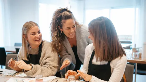 Three women laughing while painting indoors.