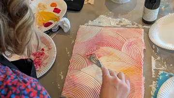 Person uses spatula on textured painting.