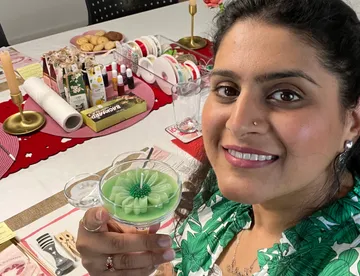 Frau hält grüne Kerze an dekoriertem Tisch.
