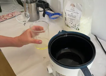Hand pouring wax near melting pot.