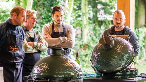 Two men cooking with ceramic grills outdoors.