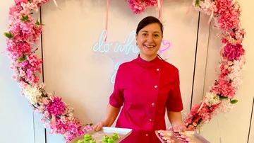 Woman in pink jacket holding pastry trays.