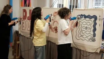 Drei Personen nutzen Tufting-Pistolen drinnen.