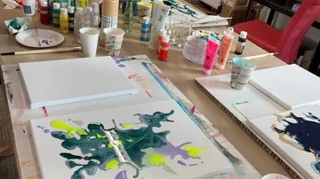 Kunstmaterialien auf Tisch mit Leinwänden.