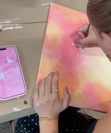 Person painting on pink canvas, phone beside.