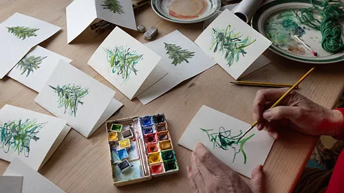 Person painting Christmas cards on table.