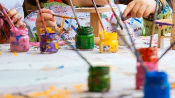 Children painting with brushes and jars of paint.