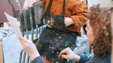 Child in apron sitting, adult showing paper.