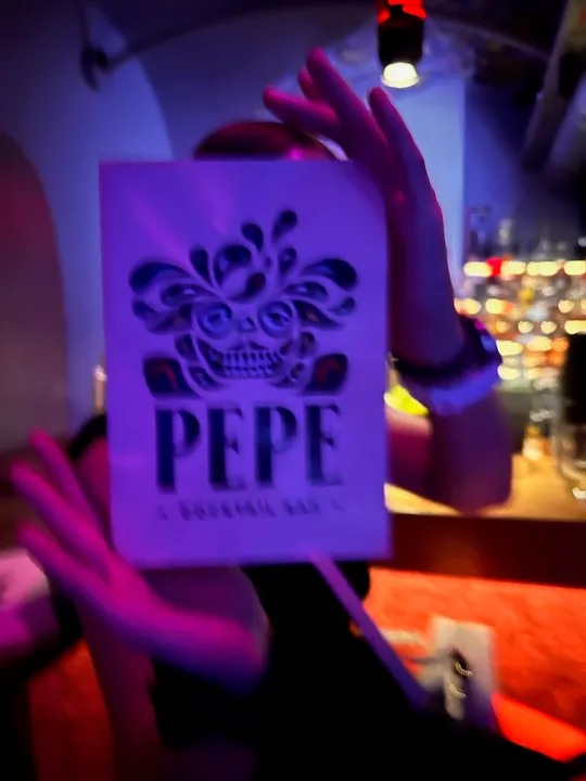 Hand holds PEPE sign in dim bar.