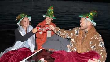 Three people with Christmas hats toasting on a boat.