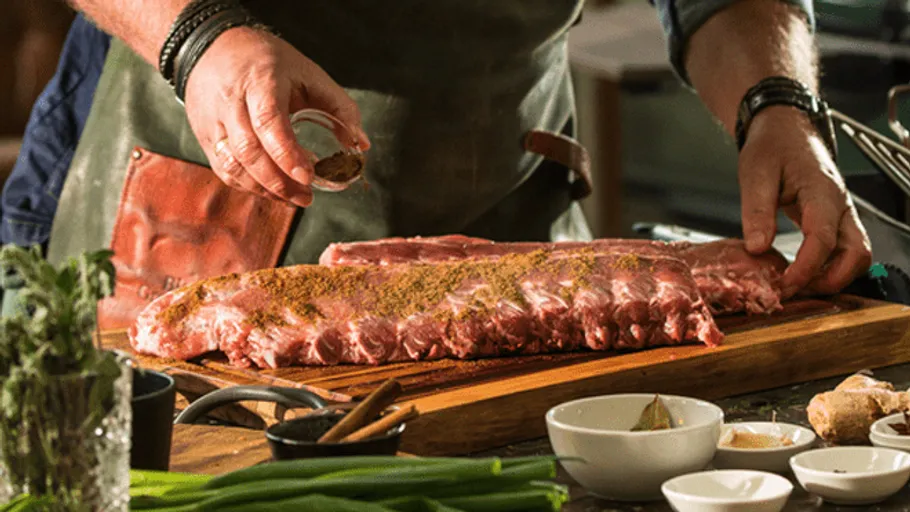 Meat pieces are seasoned with spices in a kitchen.