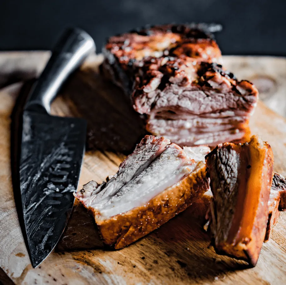 The piece of meat is cut on a wooden board with a knife.
