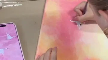 Person painting swan on orange and pink canvas.