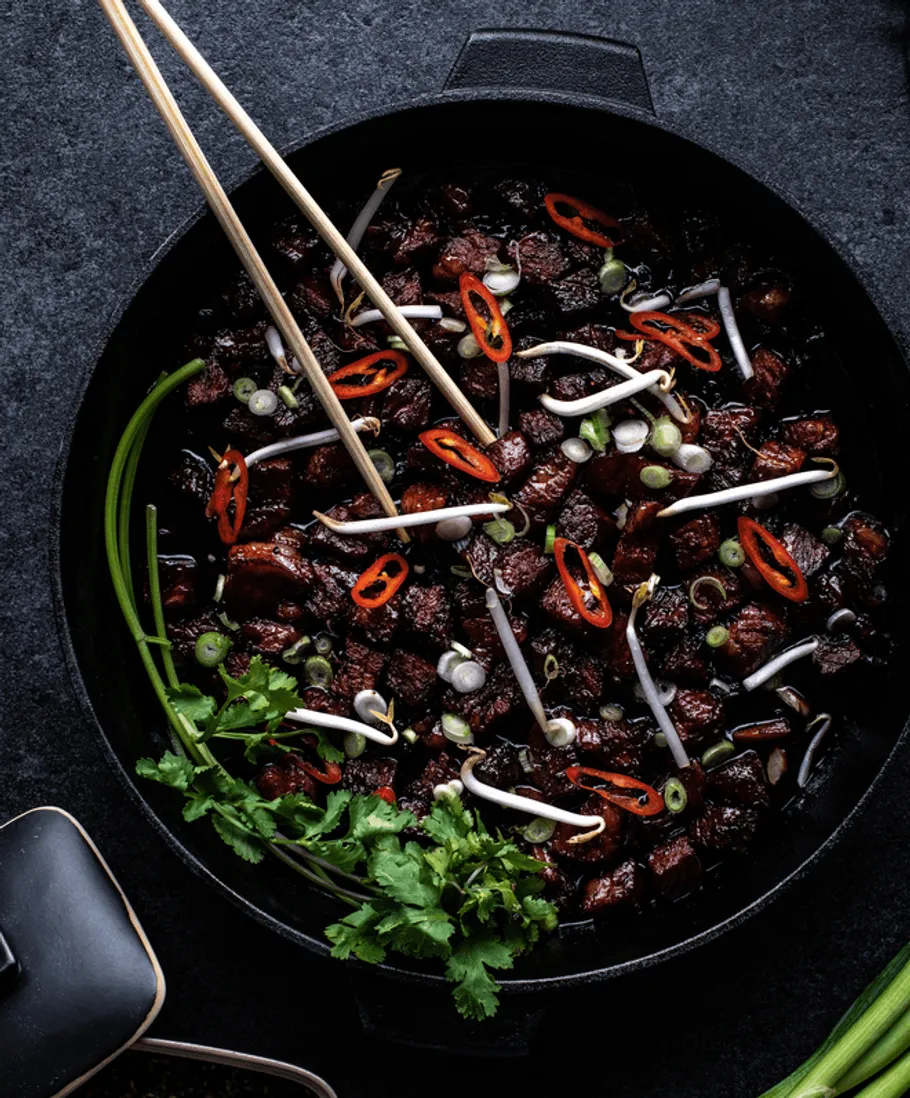 Bowl with fried meat, vegetables and chopsticks.