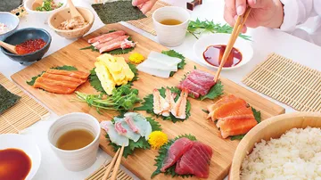 Assorted sashimi on wooden board, chopsticks selecting fish.
