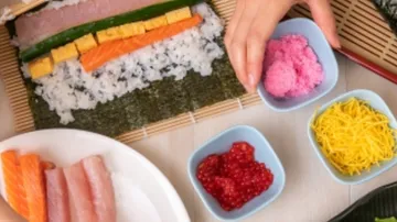 Hands rolling sushi with ingredients nearby.