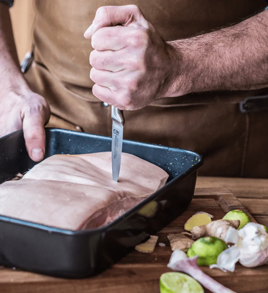 Ein Koch schneidet Fleisch in einer Auflaufform.