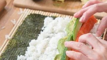 Hands rolling sushi on bamboo mat.