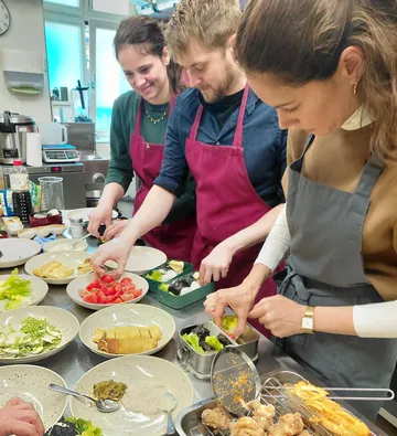 Three people chopping vegetables in kitchen.