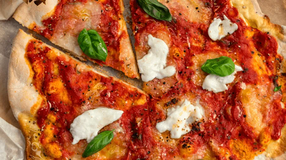 Pizza with tomato sauce, cheese and fresh basil is laid out on paper.