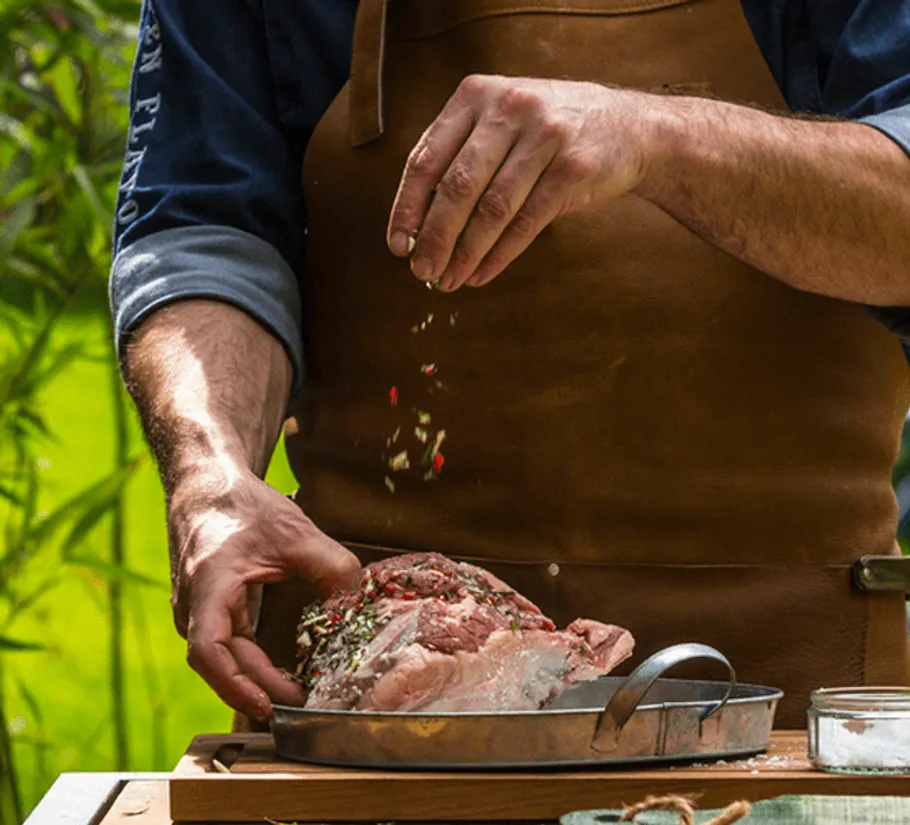 Fleisch wird gewürzt, während eine grüne Umgebung sichtbar ist.