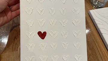 Canvas with embossed hearts, one red, on table.