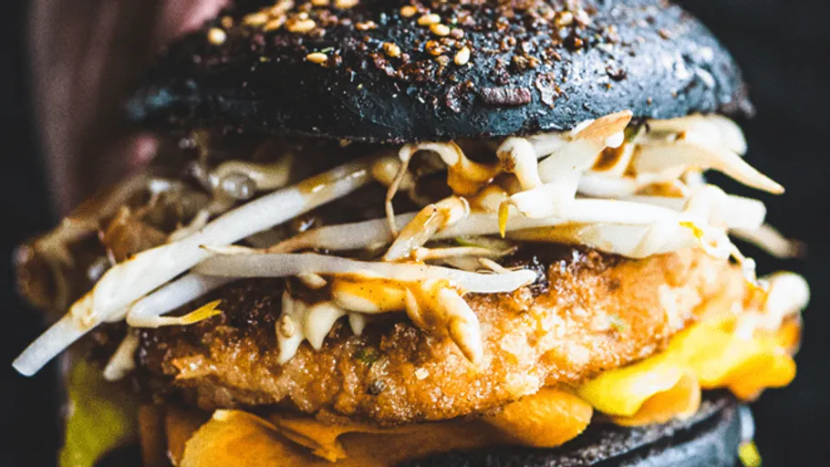 Black burger with breaded meat and vegetable filling.