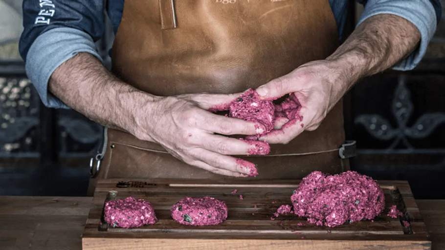 Hands form minced meat into patties on a wooden board.