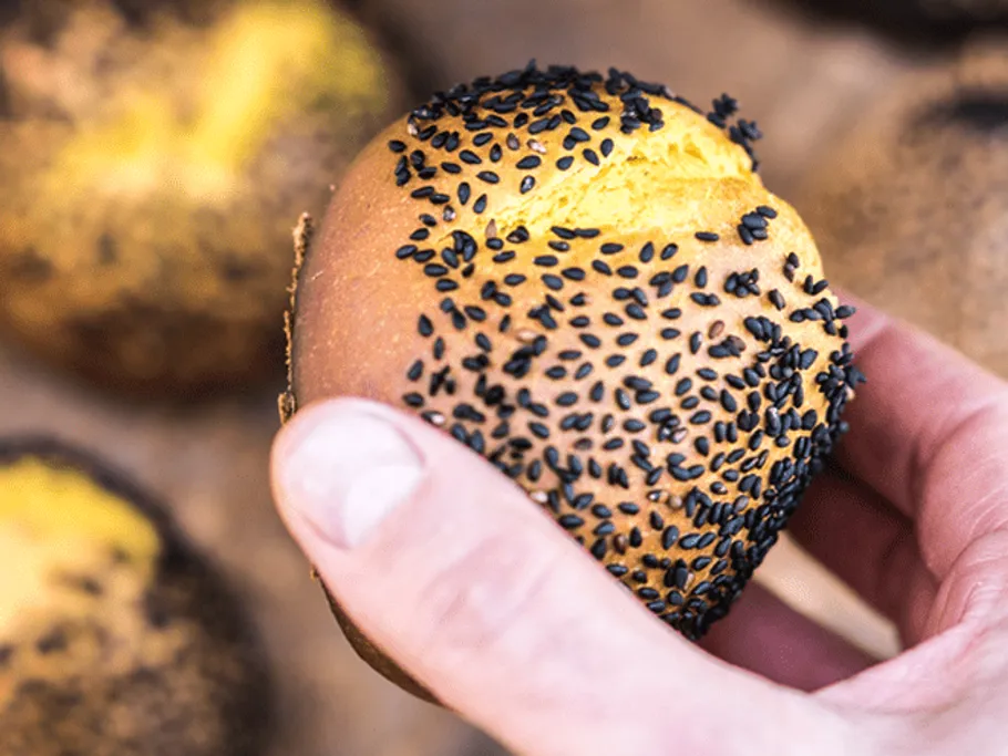 Eine Hand hält ein Brötchen mit schwarzem Sesam.
