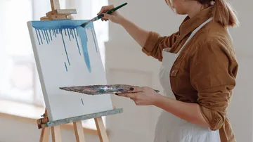 Artist painting on canvas with palette in studio.