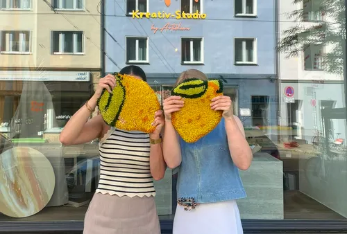 Zwei Frauen halten bunte Stoffstücke vor Studio.