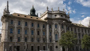 Historic building with ornate facade, trees, cloudy sky.