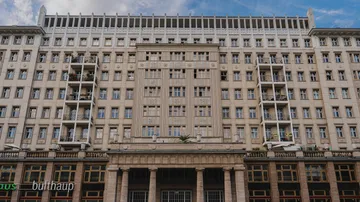 Tall building facade with balconies, cloudy sky.